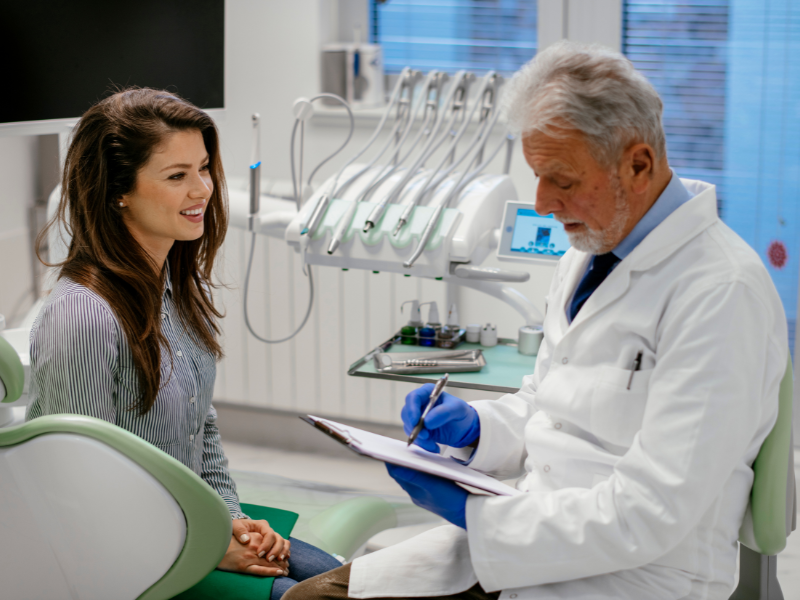 A woman speaking with her dentist in an examination room.